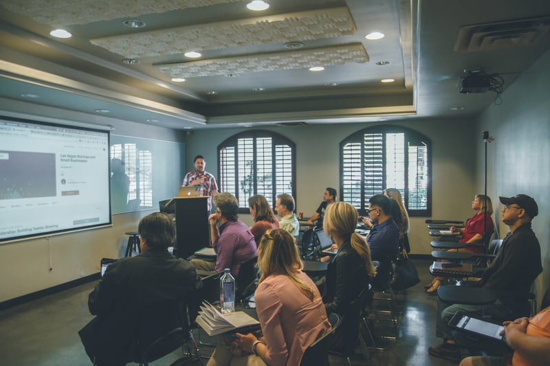 Professor presenting in a lecture hall to a group of students learning about the importance of creating spaces to discuss important and relevant topics. 